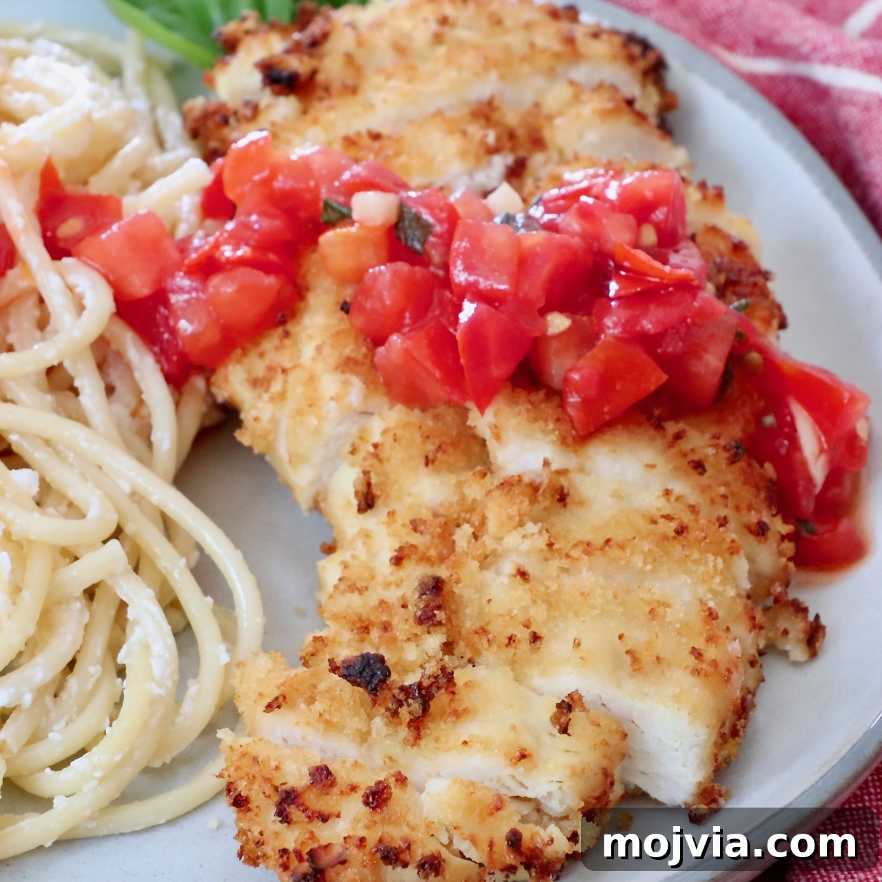 crispy chicken sliced on a plate topped with tomato bruschetta with creamy pasta noodles on the side