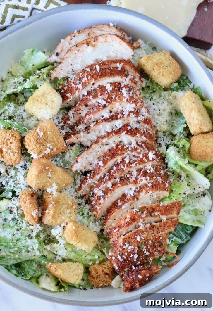 blackened chicken sliced on top of a caesar salad in a bowl with croutons