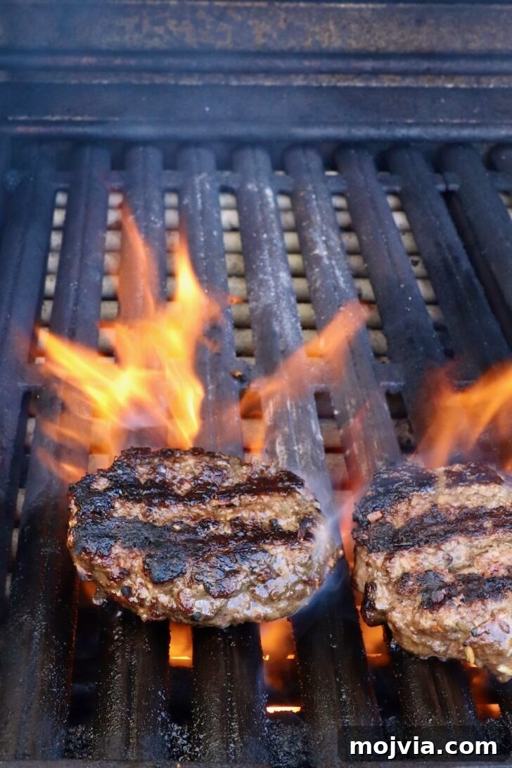 French Onion Burger Recipe with Caramelized Onions & Gruyère 8 grilled burger patties on a grill with flames