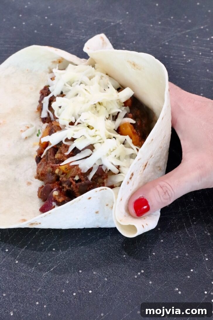 Melted Cheese, Beans & Rice Burrito Recipe for Weeknights 12 hand folding a bean and cheese burrito on a cutting board