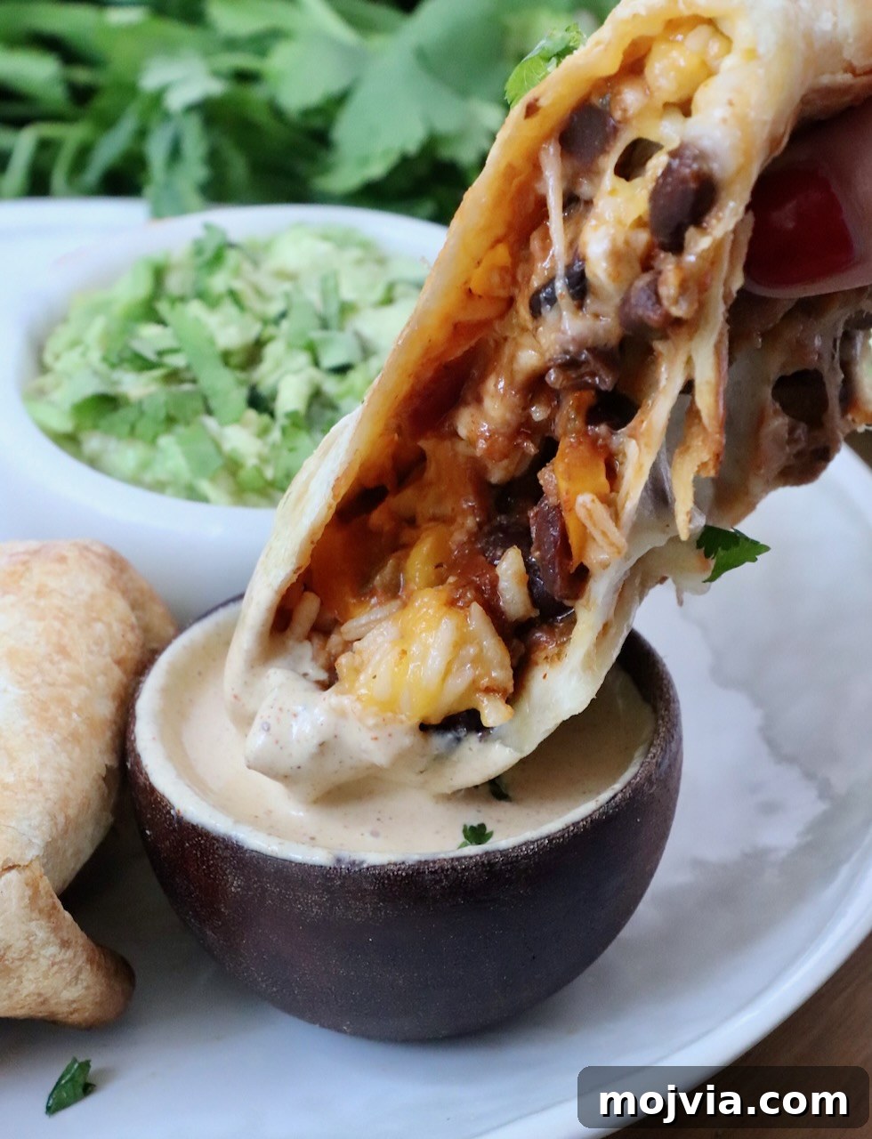 Melted Cheese, Beans & Rice Burrito Recipe for Weeknights 15 half of a burrito dipped into a small bowl of sauce with a bowl of guacamole in the background