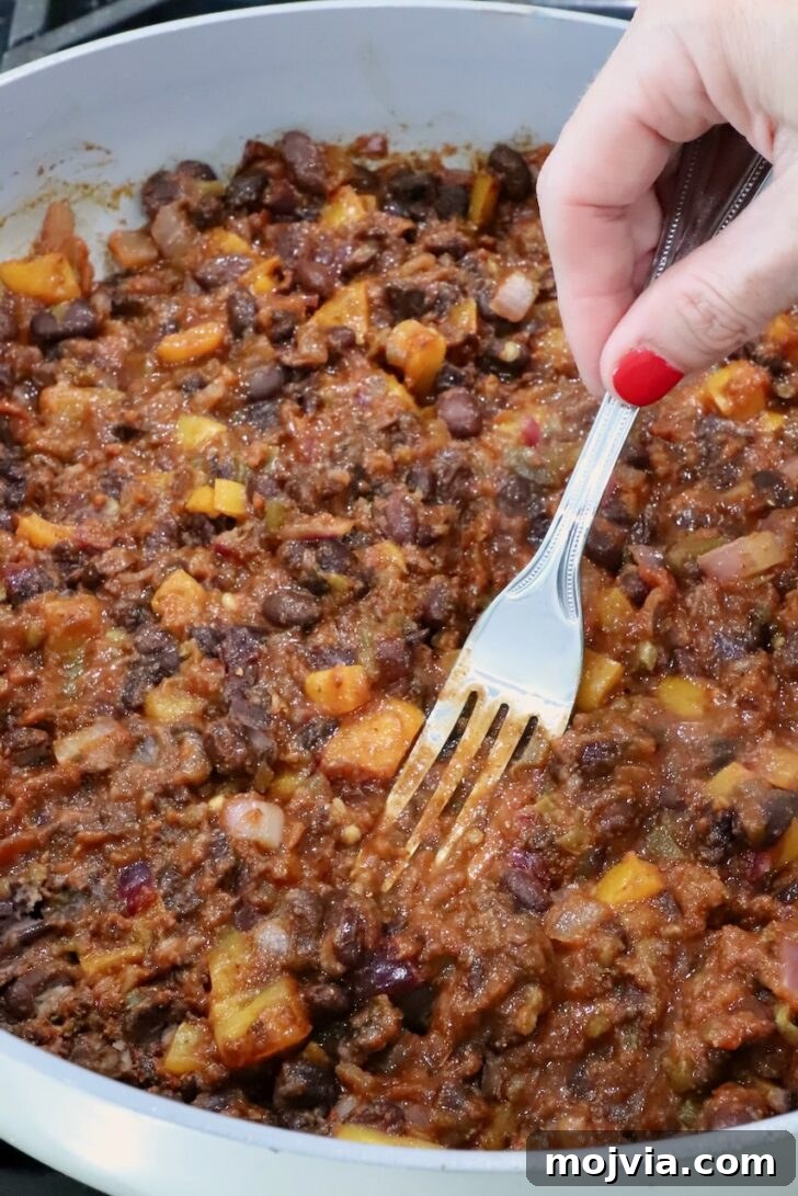 Melted Cheese, Beans & Rice Burrito Recipe for Weeknights 7 bean burrito filling in a skillet with a fork smashing the beans