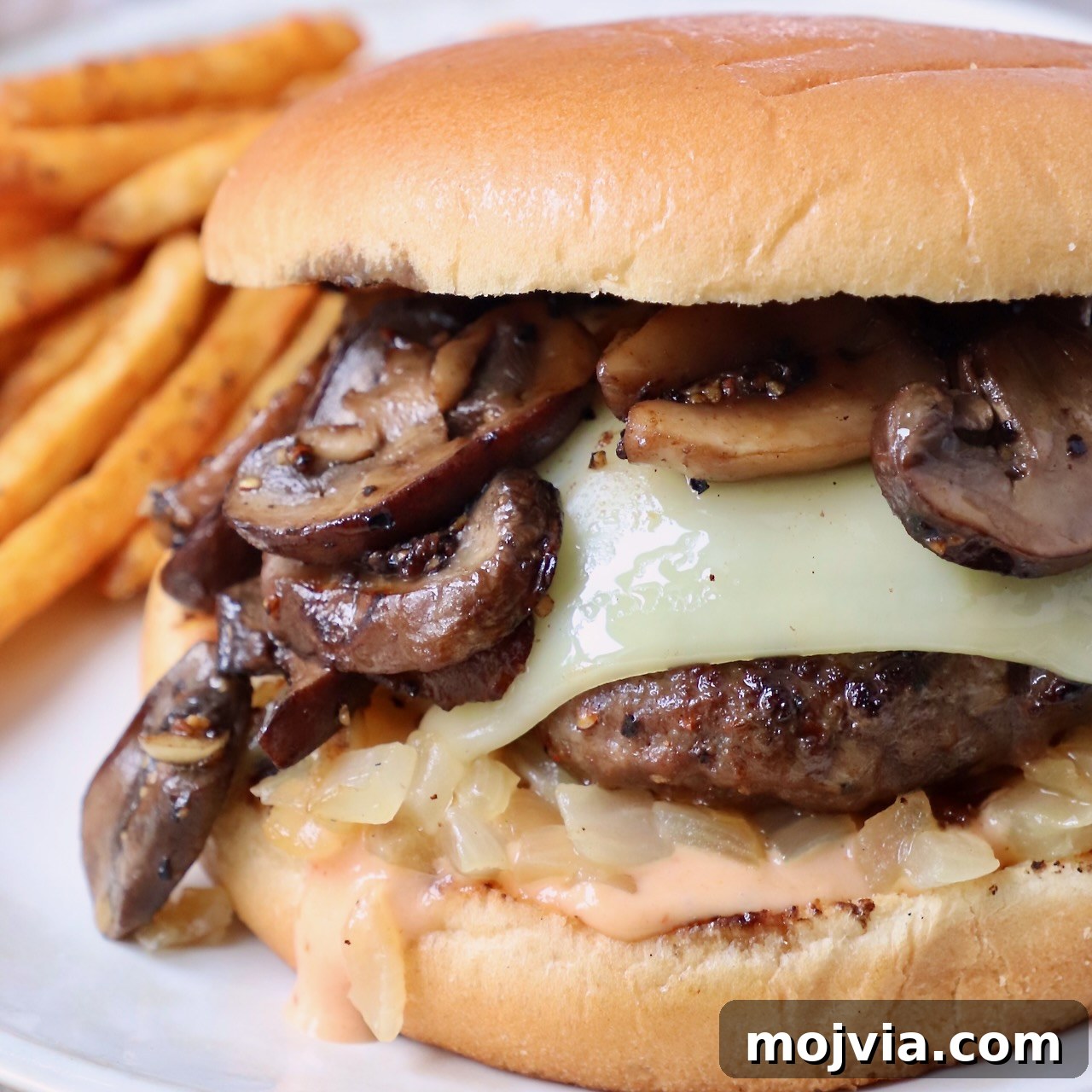 Complete Burger Guide: Techniques, Recipes & Toppings for Perfect Patties 6 cooked cheeseburger topped with sauteed mushrooms on plate with seasoned fries