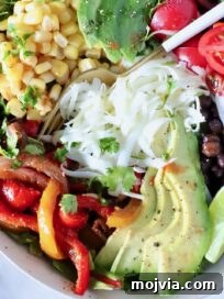 salad in a bowl topped with fajita veggies, avocado, corn, cheese, beans and tomatoes, with a fork in the middle of the bowl