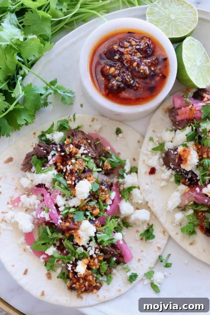 Authentic Barbacoa Seasoning Blend for Tacos and Burritos 7 shredded beef barbacoa tacos on a plate topped with salsa macha, pickled onions, and cilantro