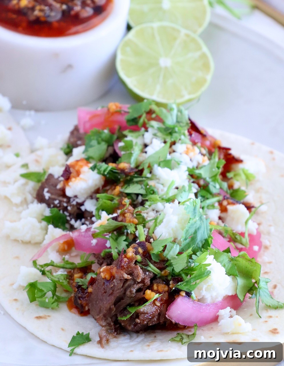 Instant Pot Beef Barbacoa: Tender Mexican Shredded Beef 12 beef barbacoa taco on a plate with salsa macha, limes, cilantro, and pickled onions