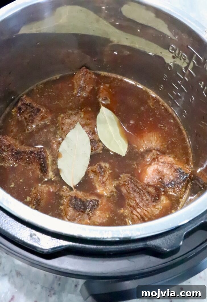 Instant Pot Beef Barbacoa: Tender Mexican Shredded Beef 8 pieces of beef, covered with beef broth and bay leaves in an Instant Pot