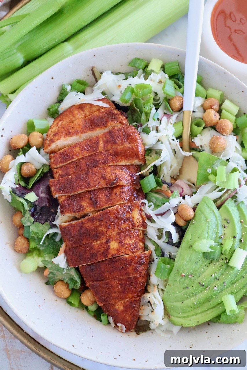 Spicy Buffalo Chicken Salad with Blue Cheese Dressing 2 sliced buffalo chicken breast on top of a salad in a bowl with sliced avocado and a fork