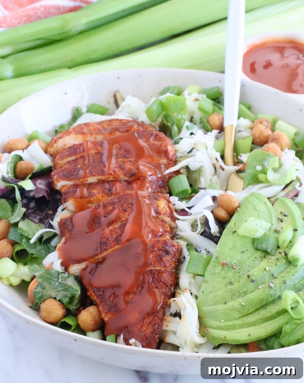 Spicy Buffalo Chicken Salad with Blue Cheese Dressing 8 sliced chicken topped with buffalo sauce on top of a salad in a bowl with sliced avocado