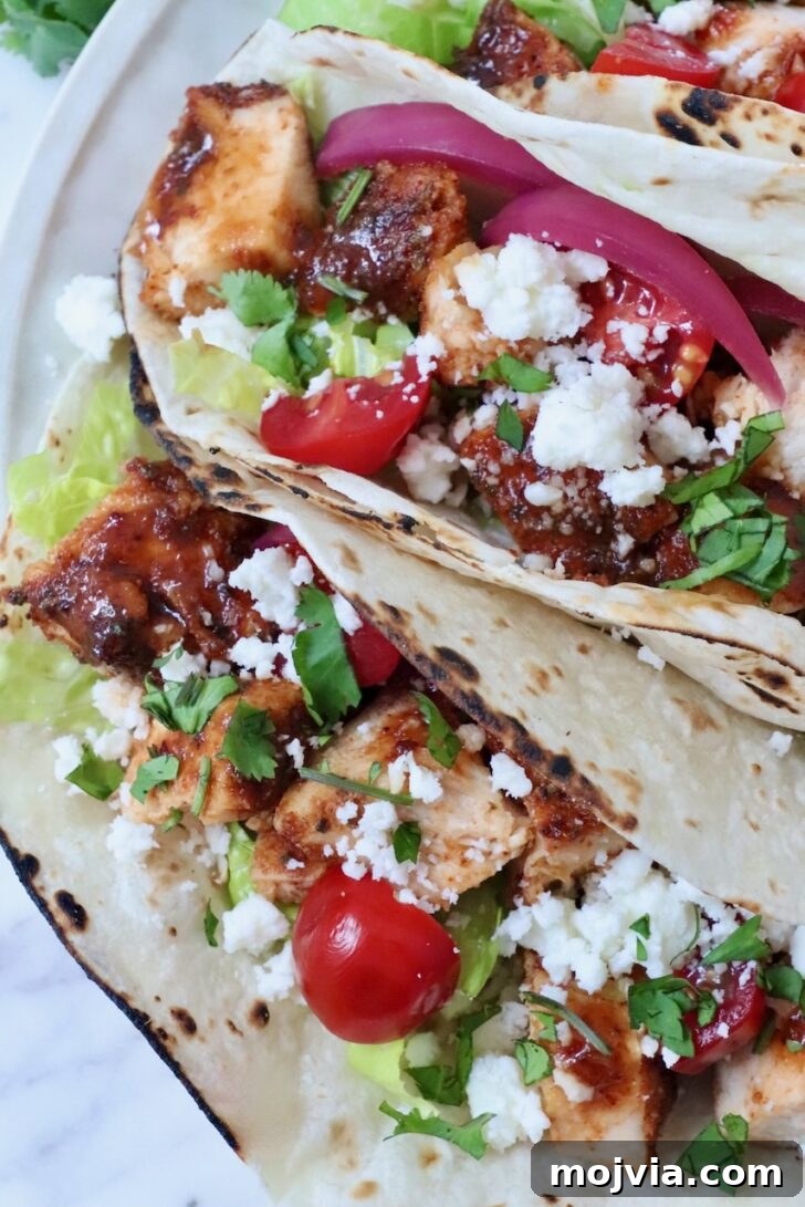 Homemade Chicken Taco Seasoning Mix for Flavorful Tacos 7 air fryer chicken tacos topped with diced tomatoes, pickled onions, cilantro, lettuce, and crumbled cheese on lightly charred tortillas.