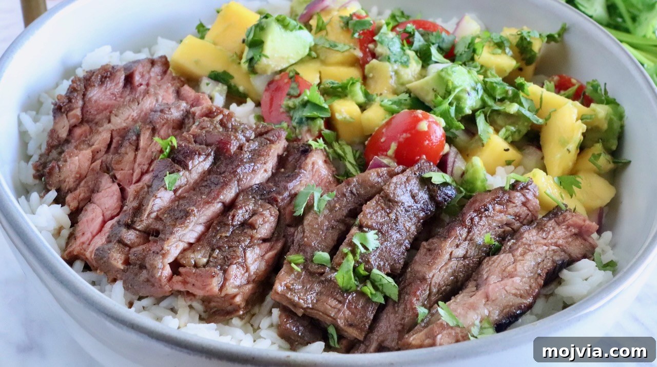 Authentic Jamaican Jerk Steak Recipe 2 sliced steak in a bowl on top of rice with mango avocado salsa