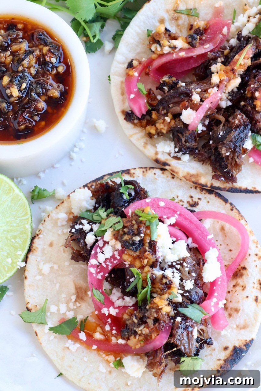 Tender Smoked Beef Cheek Barbacoa Recipe 9 smoked beef cheek tacos on a plate with salsa macha, fresh cilantro, pickled onions and a lime wedge
